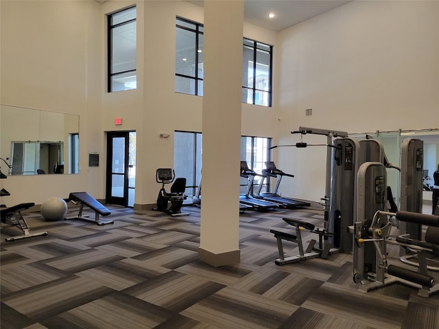 gym with a high ceiling, dark colored carpet, and visible vents