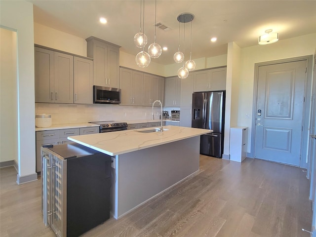 kitchen with a sink, visible vents, an island with sink, stainless steel appliances, and gray cabinetry
