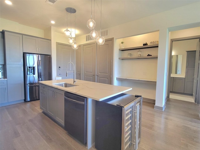 kitchen featuring open shelves, appliances with stainless steel finishes, a sink, wood finished floors, and gray cabinetry