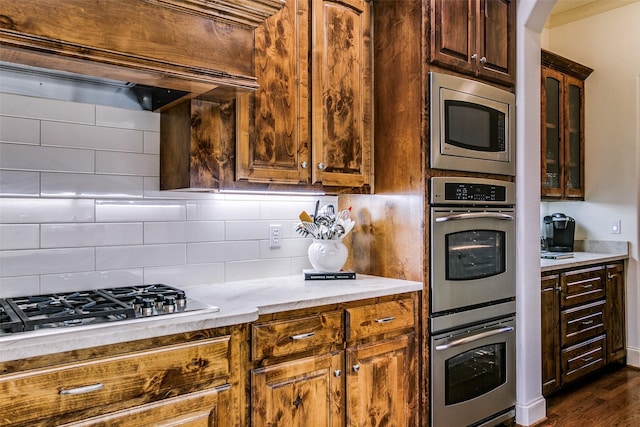 kitchen featuring light countertops, arched walkways, stainless steel appliances, tasteful backsplash, and glass insert cabinets