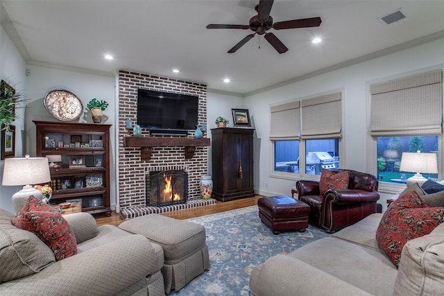 living room featuring ceiling fan, visible vents, crown molding, a fireplace, and wood finished floors