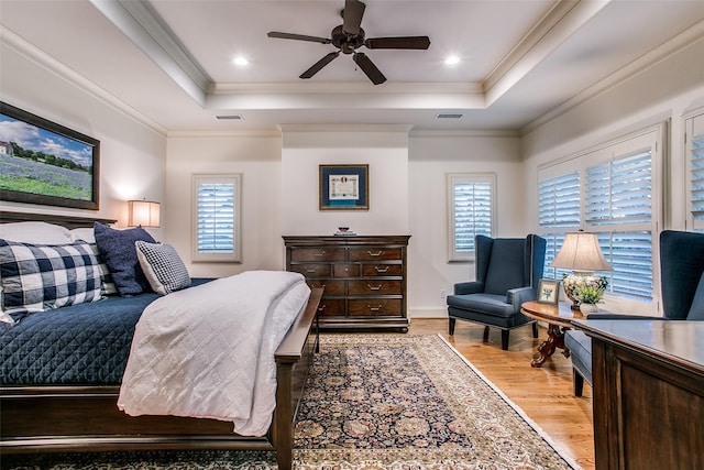 bedroom featuring light wood-style floors, a raised ceiling, visible vents, and multiple windows