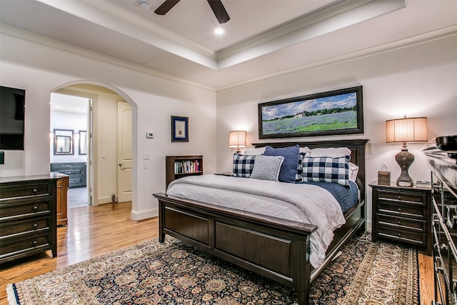 bedroom featuring a raised ceiling, arched walkways, recessed lighting, wood finished floors, and ornamental molding