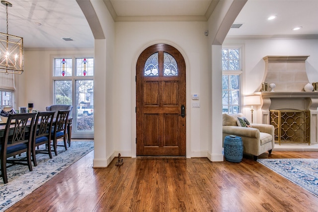 entryway with arched walkways, a wealth of natural light, wood finished floors, and a chandelier