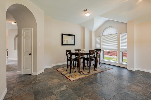 dining room with arched walkways, stone tile flooring, baseboards, and vaulted ceiling