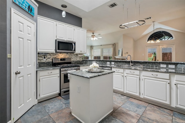 kitchen featuring appliances with stainless steel finishes, a sink, plenty of natural light, light stone finish floors, and vaulted ceiling