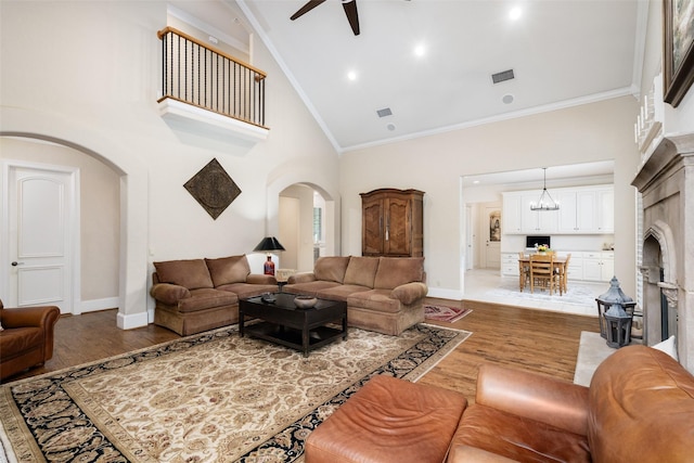living area featuring a fireplace, arched walkways, high vaulted ceiling, a ceiling fan, and wood finished floors