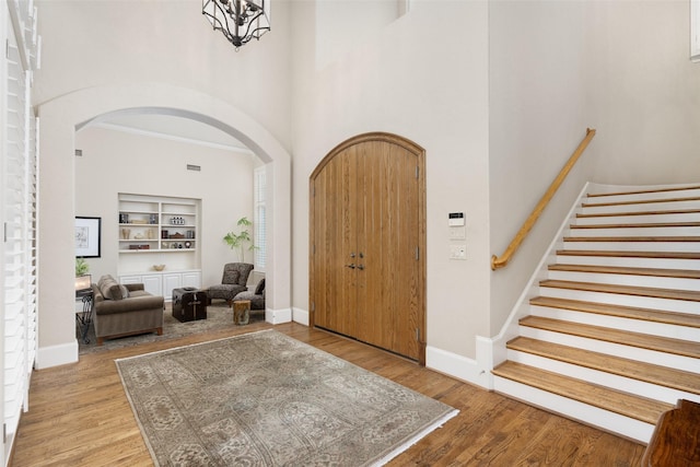 entryway featuring arched walkways, baseboards, a high ceiling, stairs, and light wood-style flooring