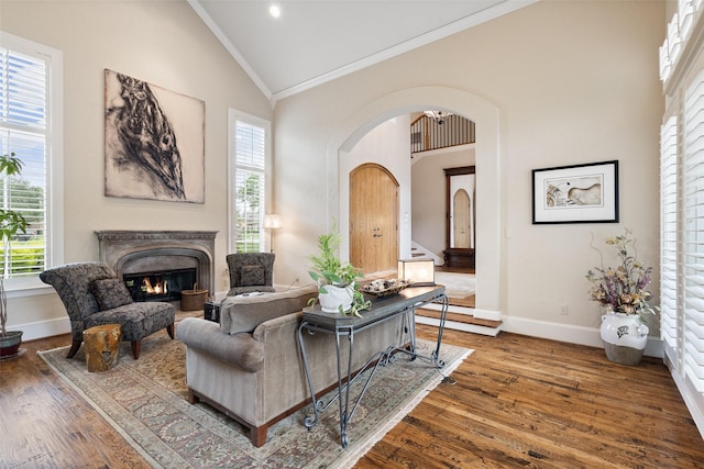living room featuring crown molding, arched walkways, a premium fireplace, baseboards, and wood finished floors