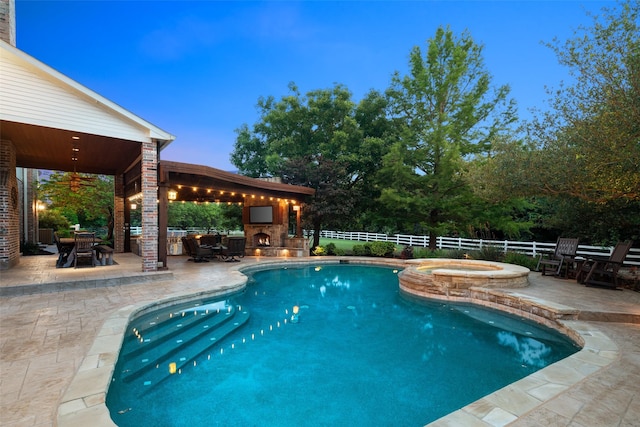 pool at dusk with outdoor dining area, a pool with connected hot tub, a warm lit fireplace, a fenced backyard, and a patio