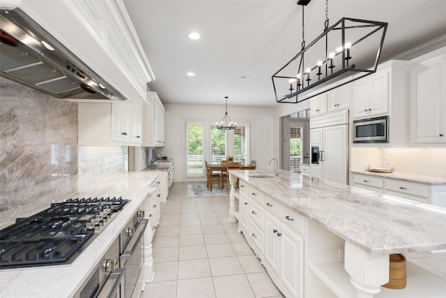 kitchen with an inviting chandelier, built in appliances, wall chimney range hood, a large island with sink, and a sink