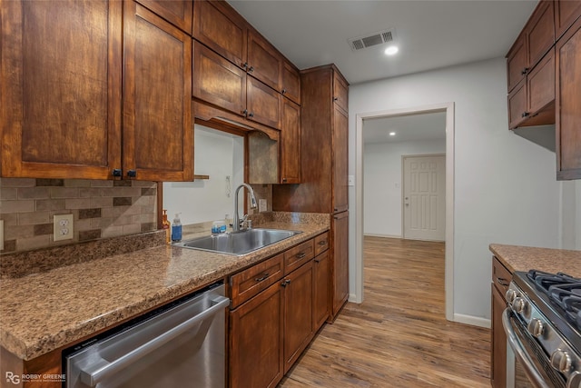 kitchen with appliances with stainless steel finishes, a sink, light wood-style flooring, backsplash, and visible vents