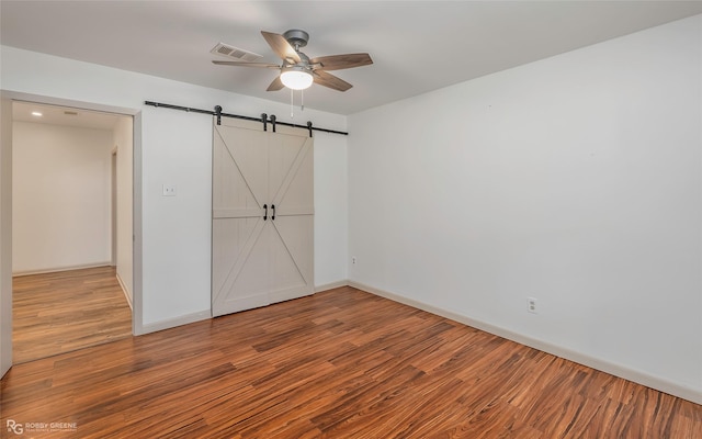 unfurnished bedroom featuring baseboards, visible vents, a barn door, and wood finished floors