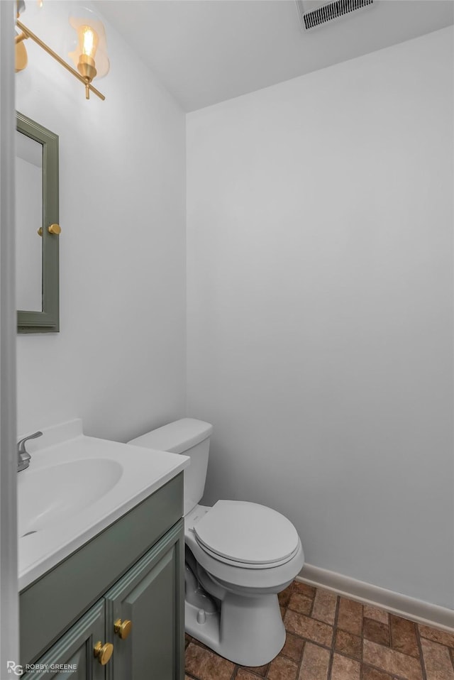 bathroom with visible vents, vanity, toilet, baseboards, and stone finish flooring