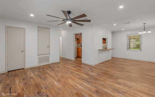 unfurnished living room featuring recessed lighting, ceiling fan with notable chandelier, and light wood finished floors