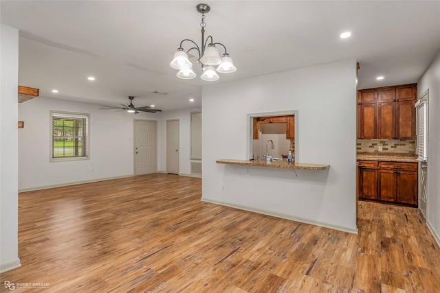 kitchen with a sink, light wood finished floors, ceiling fan with notable chandelier, recessed lighting, and tasteful backsplash