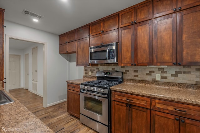 kitchen with light wood-style floors, appliances with stainless steel finishes, tasteful backsplash, and visible vents
