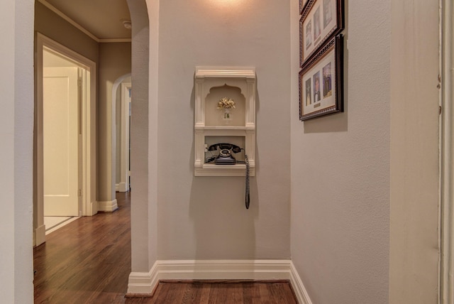 hallway featuring arched walkways, baseboards, ornamental molding, and dark wood-type flooring