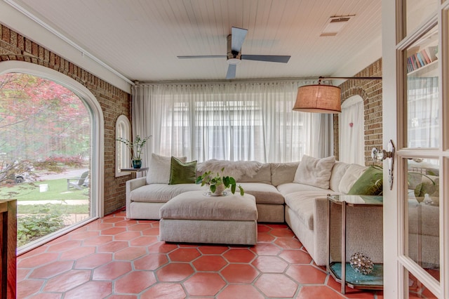 living area featuring a ceiling fan, brick wall, and a wealth of natural light