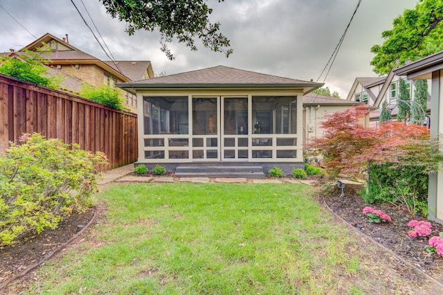 back of property with a lawn, fence, a shingled roof, and a sunroom