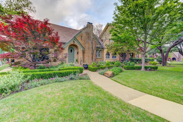 tudor house with brick siding, a chimney, and a front lawn