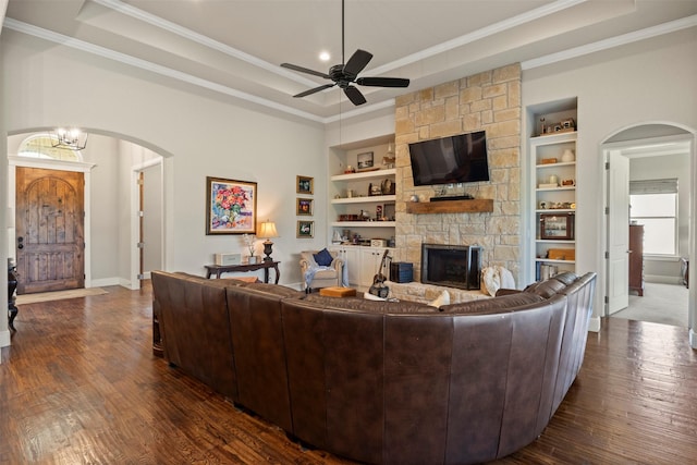 living room with crown molding, arched walkways, a fireplace, and a raised ceiling