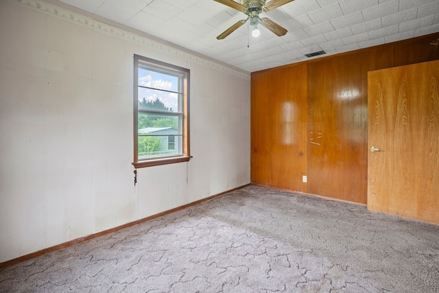 carpeted spare room featuring visible vents, ceiling fan, and wooden walls