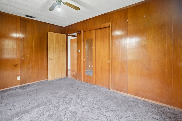 unfurnished bedroom with wooden walls, carpet floors, a ceiling fan, and visible vents