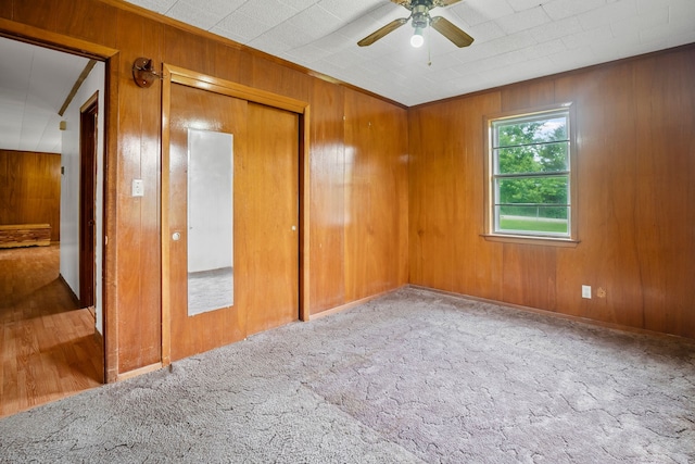 unfurnished bedroom featuring carpet flooring, ceiling fan, wood walls, and a closet