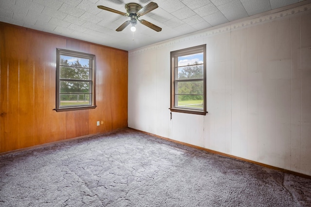 carpeted spare room with ceiling fan, wood walls, and baseboards