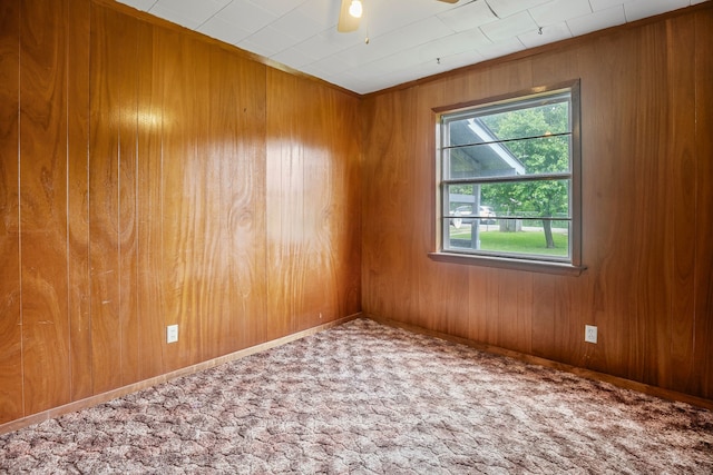 carpeted empty room with wooden walls and a ceiling fan