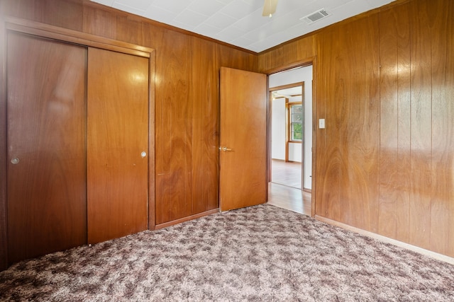unfurnished bedroom featuring a closet, carpet floors, visible vents, ceiling fan, and wooden walls