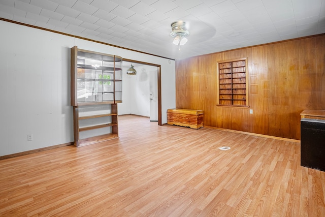 empty room featuring ceiling fan, wood walls, wood finished floors, baseboards, and ornamental molding