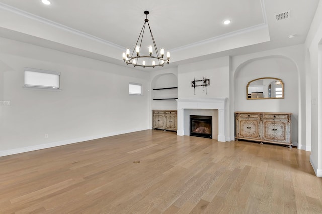 unfurnished living room featuring visible vents, a glass covered fireplace, a tray ceiling, a chandelier, and light wood-style flooring
