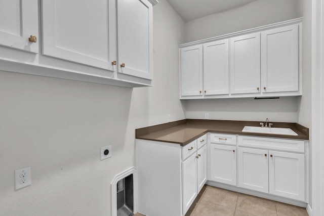 laundry area featuring cabinet space, light tile patterned flooring, hookup for an electric dryer, and a sink