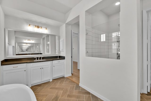 full bathroom with baseboards, a freestanding bath, tiled shower, and vanity