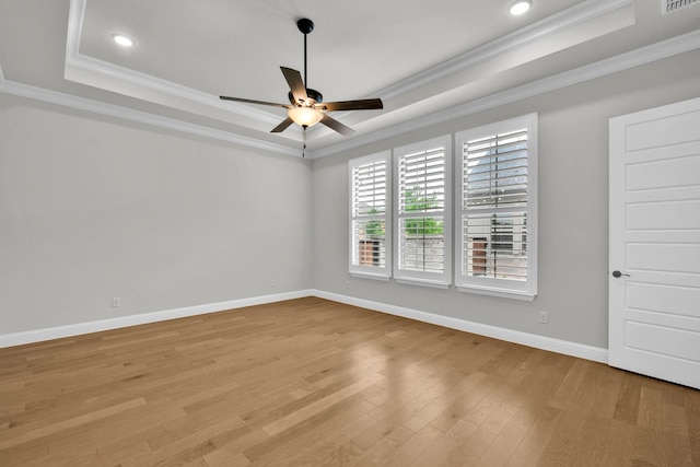 empty room with crown molding, light wood-style floors, baseboards, a tray ceiling, and a ceiling fan