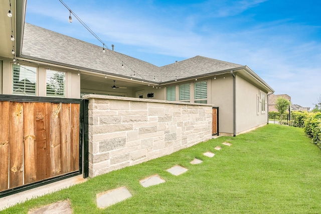 rear view of property with a lawn, a shingled roof, and stucco siding