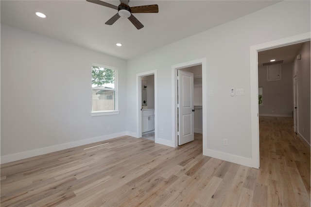 unfurnished bedroom with baseboards, a walk in closet, ensuite bathroom, and light wood-type flooring