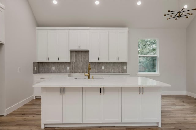 kitchen with backsplash, white cabinetry, baseboards, and a sink