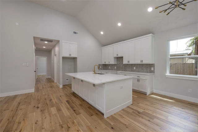 kitchen with white cabinets, light wood-style flooring, decorative backsplash, visible vents, and a center island with sink