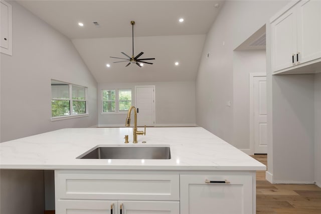 kitchen with a sink, light stone counters, ceiling fan, and light wood-style floors
