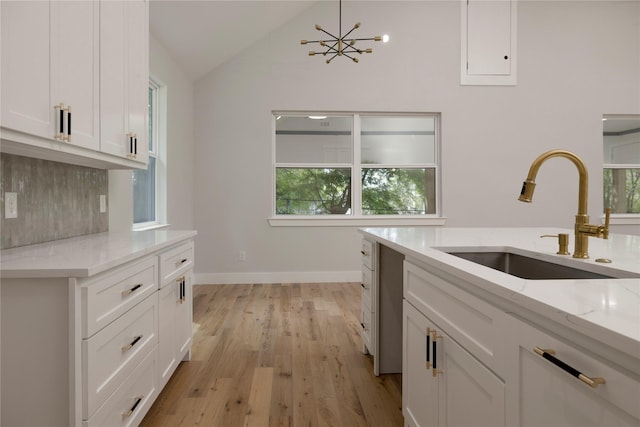 kitchen with white cabinets, light stone countertops, a sink, light wood-style flooring, and lofted ceiling