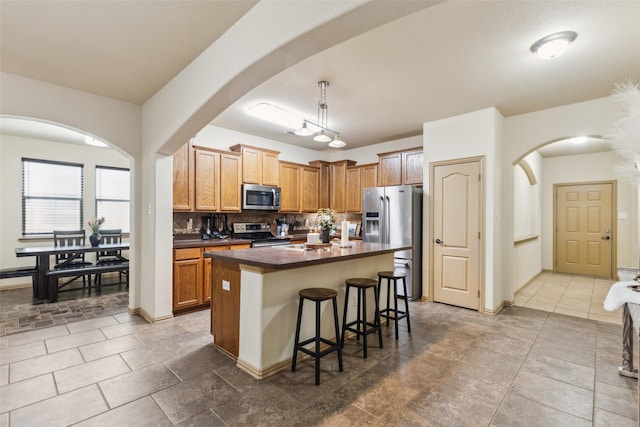1925 Bridgeport Dr, Providence Village, TX 76227 - kitchen with decorative backsplash, a kitchen bar, dark countertops, appliances with stainless steel finishes, and arched walkways