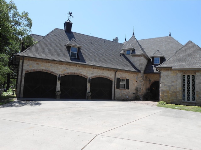french country inspired facade featuring a high end roof, an attached garage, concrete driveway, and stone siding