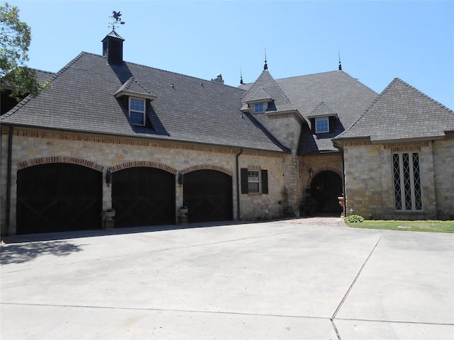 french country home featuring a garage, a high end roof, driveway, and stone siding