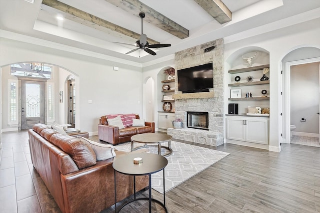 living room with ceiling fan, beam ceiling, a fireplace, arched walkways, and baseboards