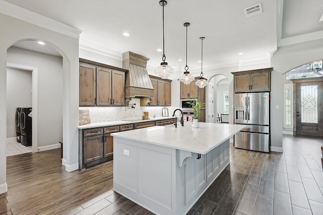 kitchen with washer and dryer, stainless steel fridge with ice dispenser, arched walkways, custom range hood, and visible vents