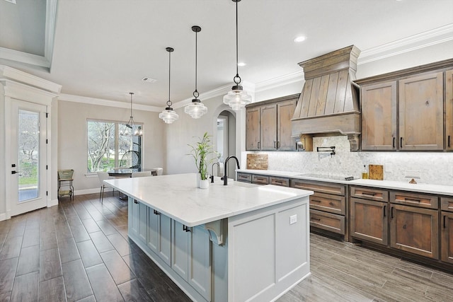 kitchen featuring a kitchen island with sink, arched walkways, custom range hood, and tasteful backsplash