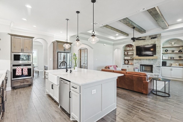 kitchen with ceiling fan, appliances with stainless steel finishes, a sink, arched walkways, and a stone fireplace